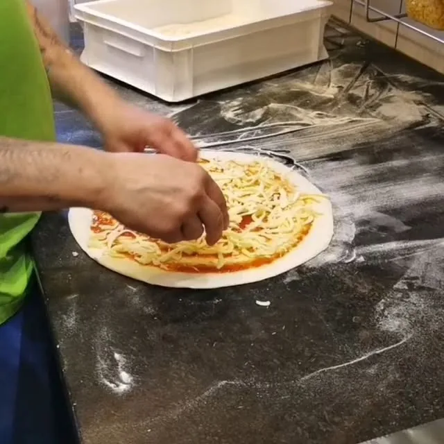 Ruky sypú syr na tenké cesto s paradajkovým základom